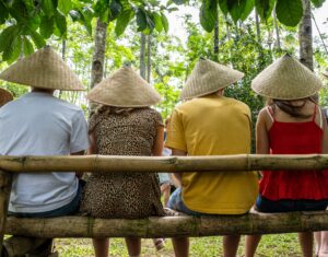 e wearing Asian conical hats while sitting on a bamboo bench